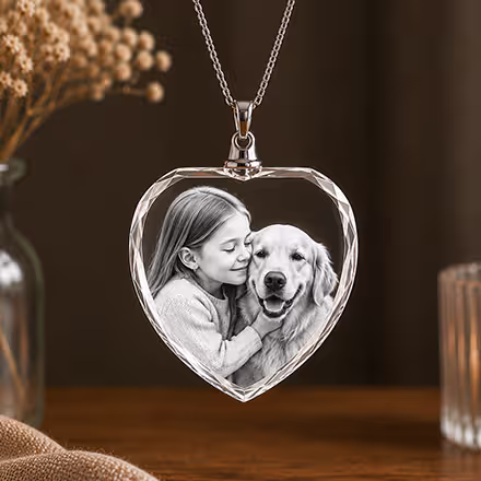 2D Crystal Heart Necklace engraved with a young girl and Golden Retriever portrait, suspended from a silver chain in a warm home setting.